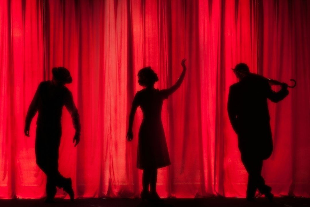 Tre silhuetter framför en röd teatergardin, som i en musikalfinal